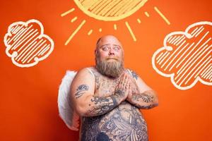 Fat amazed man with beard ,tattoos and wings acts like an angel photo