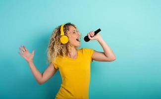 Girl with headset listens to music and song with microphone. emotional and energetic expression. Cyan background photo