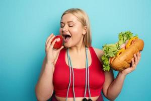 Fat girl prefers to eat an apple instead of a big sandwich. cyan background photo