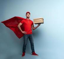 Deliveryman with pizzas acts like a powerful superhero. Concept of success and guarantee on shipment. Studio cyan background photo