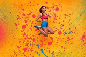 deporte mujer saltos en un amarillo antecedentes. contento y alegre expresión. rociar efecto foto