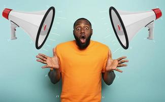 Amazed and shocked expression of a boy who receive a message with loudspeakers over cyan background photo