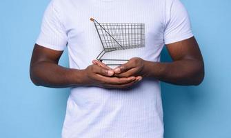 Black man with white t-shirt holds a shopping cart. cyan background photo