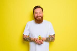 Happy man with beard and tattoos holds an avocado photo