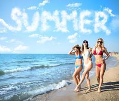 Group of happy friends having fun at ocean beach with summer word made of clouds photo