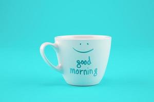 White cup of coffee on a cyan background with a wish for a good day. photo