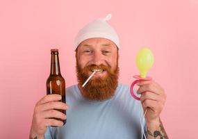 Happy man with beard and tattoos acts like a little newborn baby with beer in hand photo