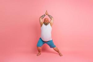 Funny man with beard in yoga position on studio pink background photo