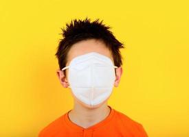 Child covers all face with the mask for covid-19 coronavirus. yellow background photo