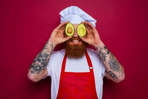 happy chef with beard and red apron holds an avocado photo