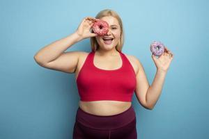 Fat woman eats sweet instead of do gym. Cyan background photo