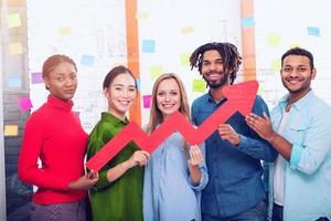 Young happy and colorful business team hold a red statistical arrow. Concept of growing, succesful and profit photo