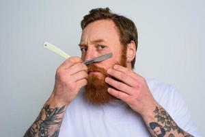 Serious man with blade is focused on cutting his beard photo