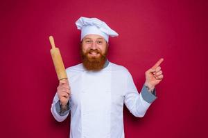 happy chef with beard and red apron chef holds wooden rolling pin photo