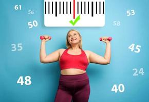 Fat girl does gym at home with satisfied expression because she decrease her weight. Cyan background photo