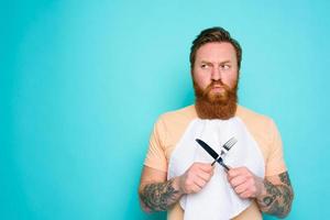 hombre con tatuajes es Listo a comer con cuchillería en mano con algunos duda foto
