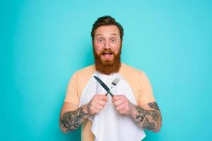 Happy man with tattoos is ready to eat with cutlery in hand photo