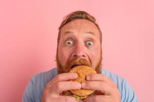 Hungry man with beard and tattoos eats a sandwitch with hamburger photo