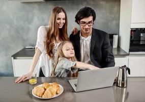 contento pequeño niña acecho un película en el computadora con su padre y madre foto