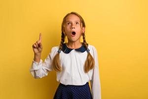 Young student is with shocked expression and indicates something. Yellow background photo