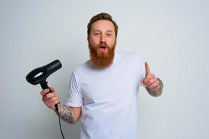 contento hombre con barba utilizar pelo secadora como micrófono y bailes foto
