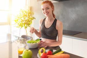 atlético joven rojo peludo mujer en el hogar cocina comiendo un sano ensalada foto