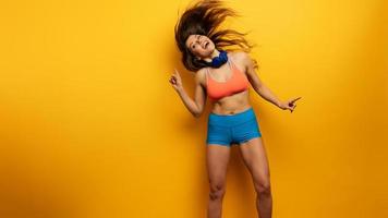 Fitness girl listens to music with headset. Joyful and happy expression on yellow background photo