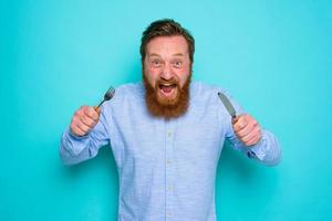 Hungry man with tattoos is ready to eat with cutlery in hand photo