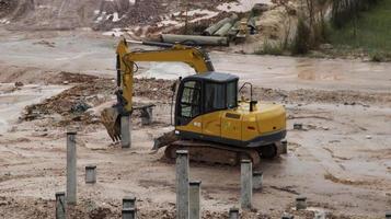 An excavator is working to insert stake or concrete foundation pillars into the ground on a construction site project. photo