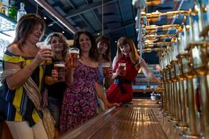 group of smiling mature women is drinking beer in a pub in front of a beer tap photo