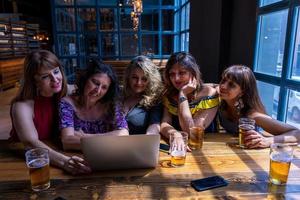grupo de hembra amigos teniendo divertido Bebiendo cerveza y acecho computadora en un pub foto