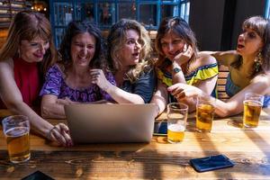 grupo de hembra amigos teniendo divertido Bebiendo cerveza y acecho computadora foto