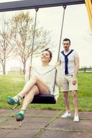 young man pushes her girlfriend on the swing photo