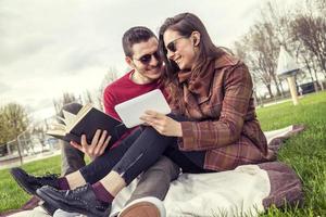 nice couple boyfriends relaxing on meadow looking at book and smart phone photo