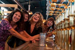 grupo de maduro mujer es Bebiendo cerveza en un pub en frente de un cerveza grifo foto