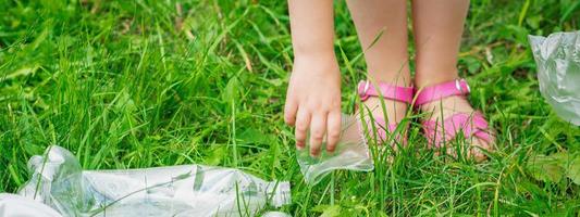 la mano del niño limpia la hierba verde de la basura plástica foto