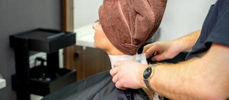 Hairdresser puts on black cape to female customer photo