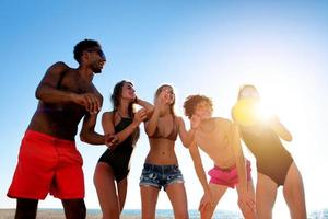 grupo de contento amigos teniendo divertido a Oceano playa a amanecer foto