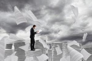 Businessman at work over a pile of paper towers of worksheets photo