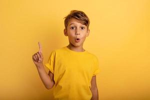 Child indicates above. Amazed and shocked expression. Yellow background photo