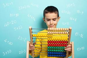 Child tries to solve mathematical problem with abacus. Cyan background photo