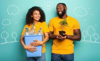 Happy couple hold a plastic container with bottles and a small tree over a light blue color. Concept of ecology, conservation, recycling and sustainability photo