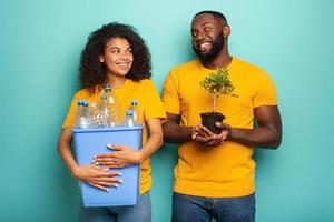 Happy couple hold a plastic container with bottles and a small tree over a light blue color. Concept of ecology, conservation, recycling and sustainability photo