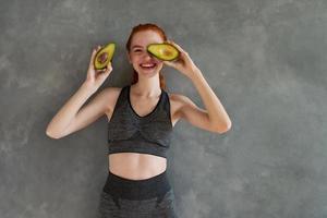 Athletic girl with gym clothes eats avocado at home photo