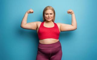 Fat girl does gym at home. satisfied expression. Cyan background photo