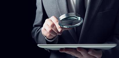 Businessman examines a tablet with a magnifying glass. Concept of internet security photo