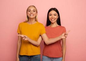 dos muchachas indica algo. alegre expresión rostro. rosado antecedentes con blanco espacio para tu texto foto