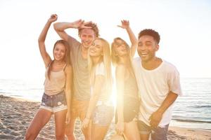 grupo de contento amigos teniendo divertido a Oceano playa a amanecer foto