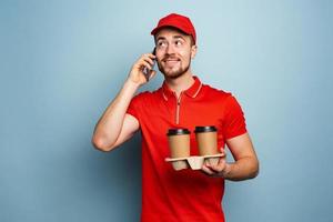 Courier delivers hot coffee and receive call on phone. Cyan background photo