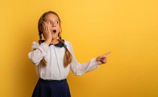 Young student is with shocked expression and indicates something. Yellow background photo